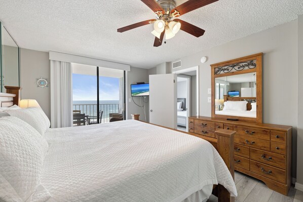 A hotel room with a bed, a dresser, a ceiling fan, a television, and a view of the ocean. - Sunswept 807 Penthouse by Liquid Life (Orange Beach)