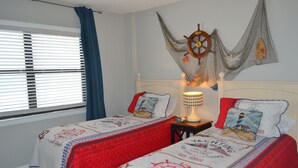 Een kamer met twee bedden, een aan de muur bevestigd scheepsrad en een lamp op een nachtkastje.