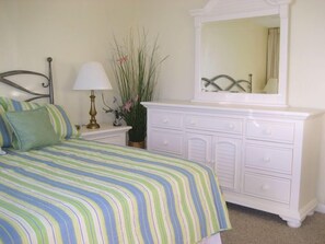 A bedroom with a bed, a nightstand, a dresser, a mirror, and a lamp. - Seaside Beach & Racquet 3702 by Liquid Life (Orange Beach)