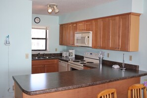 A kitchen with wooden cabinets, a microwave, a stove, and a coffee maker. - Seaside Beach & Racquet 3702 by Liquid Life (Orange Beach)