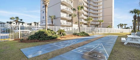 A courtyard with a shuffleboard court, palm trees, and a white fence.