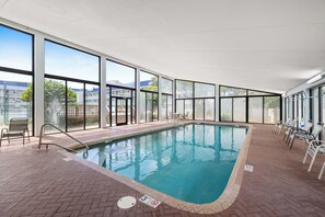 An indoor swimming pool with clear glass walls, a brick floor, and a poolside area with chairs. - Seaside Beach & Racquet 3702 by Liquid Life (Orange Beach)
