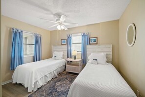 Ein Hotelzimmer mit zwei Einzelbetten, einem Deckenventilator, einem Nachttisch mit Lampe und einem kleinen Tisch.