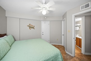 A bedroom with a bed, a ceiling fan, a door, and a bathroom visible through an open door. - Seaside Beach & Racquet 5414 by Liquid Life (Orange Beach)