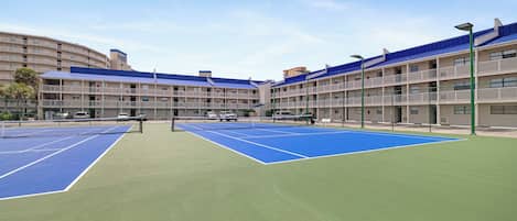 Ein Tennisplatz mit Netz in der Mitte, umgeben von einem Gebäude mit Balkonen und einem blauen Dach.
