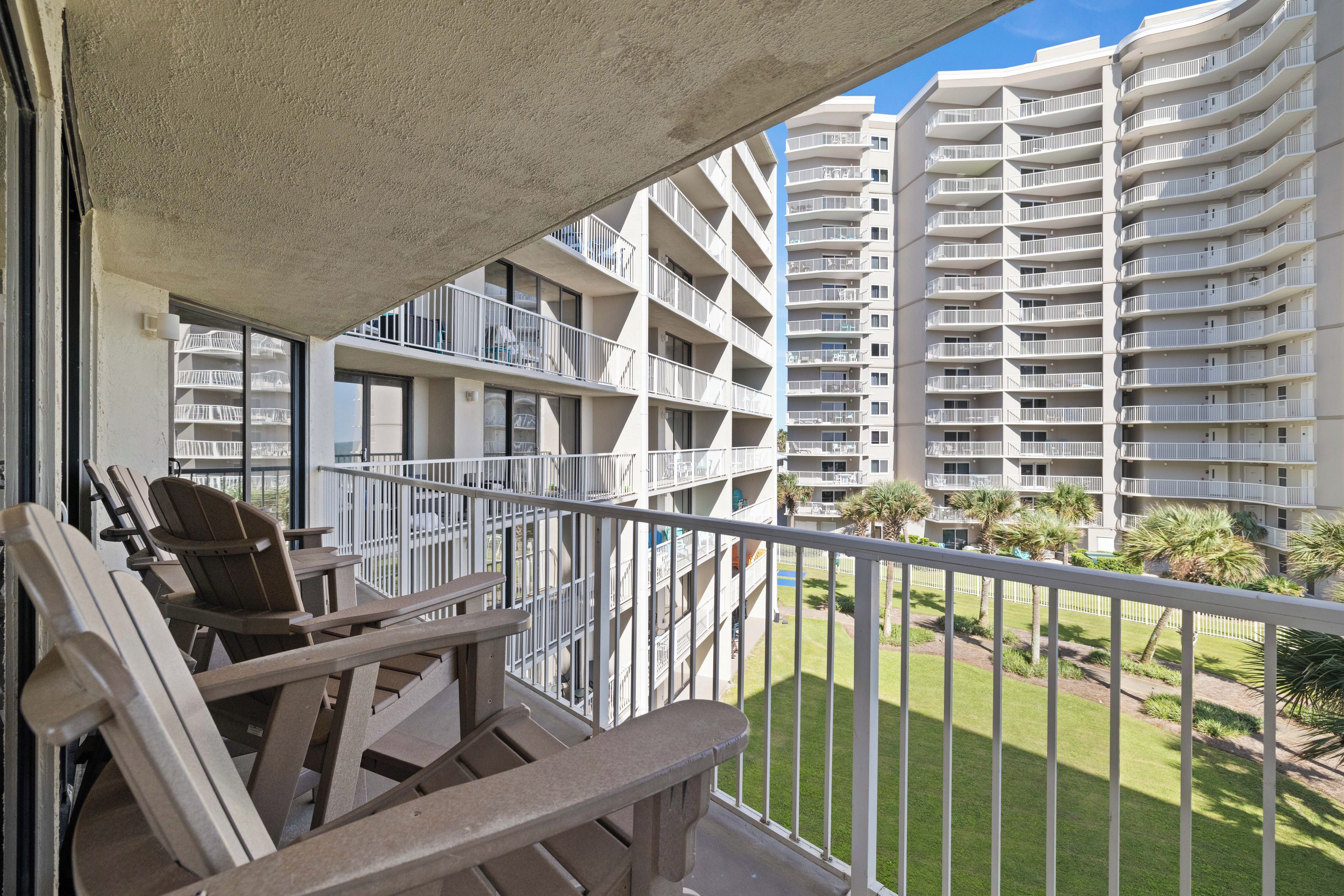 A balcony with outdoor furniture, a view of a high-rise building, and a well-maintained lawn.