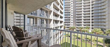 A balcony with outdoor furniture, a view of a high-rise building, and a well-maintained lawn.