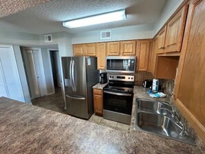 A kitchen with stainless steel appliances, wooden cabinets, and a granite countertop. - Seaside Beach & Racquet 5414 by Liquid Life (Orange Beach)