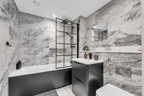 Ein modernes Badezimmer mit Marmorwand, einer freistehenden Badewanne, einer Duschkabine und einem eingebauten Waschtisch.