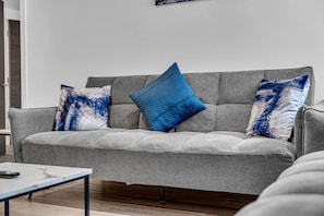 A grey sofa with three cushions, one blue and two with a blue and white abstract design, in a modern living room with a wooden coffee table. - Spacious & Modern Anfield Flat | WiFi | Sleeps 4 (Anfield)