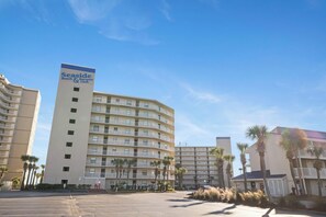 Ein Hotel des Seaside Beach & Racquet Club mit einer geschwungenen Fassade, mehreren Balkonen und Palmen im Vordergrund.