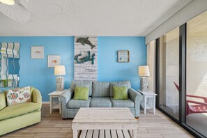 Ein Wohnzimmer mit blauer Wand, einem gestreiften Sofa, einem grünen Sessel und einem Couchtisch aus Holz.