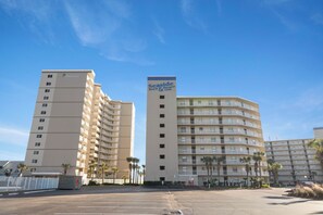 A Seaside Beach Resort building with multiple floors, balconies, and a parking lot in front. - Seaside Beach & Racquet 5915 by Liquid Life (Orange Beach)