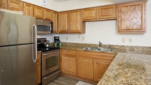 A kitchen with wooden cabinets, stainless steel appliances, a granite countertop, and a clock on the wall. - Seaside Beach & Racquet 5915 by Liquid Life (Orange Beach)
