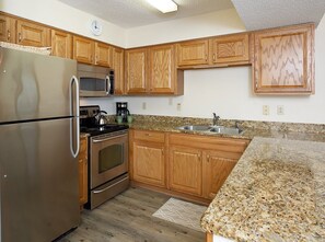 A kitchen with wooden cabinets, stainless steel appliances, a granite countertop, and a clock on the wall. - Seaside Beach & Racquet 5915 by Liquid Life (Orange Beach)
