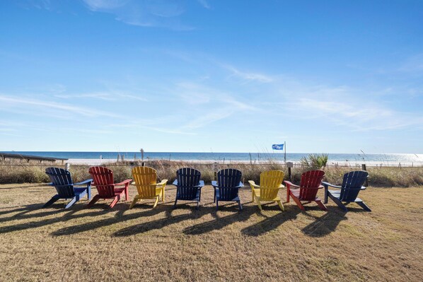 A row of colorful Adirondack chairs facing a beach with a clear sky. - Seaside Beach & Racquet 5915 by Liquid Life (Orange Beach)