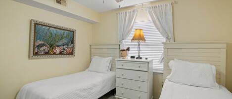 A bedroom with two single beds, a ceiling fan, a nightstand with a lamp, and a painting on the wall.
