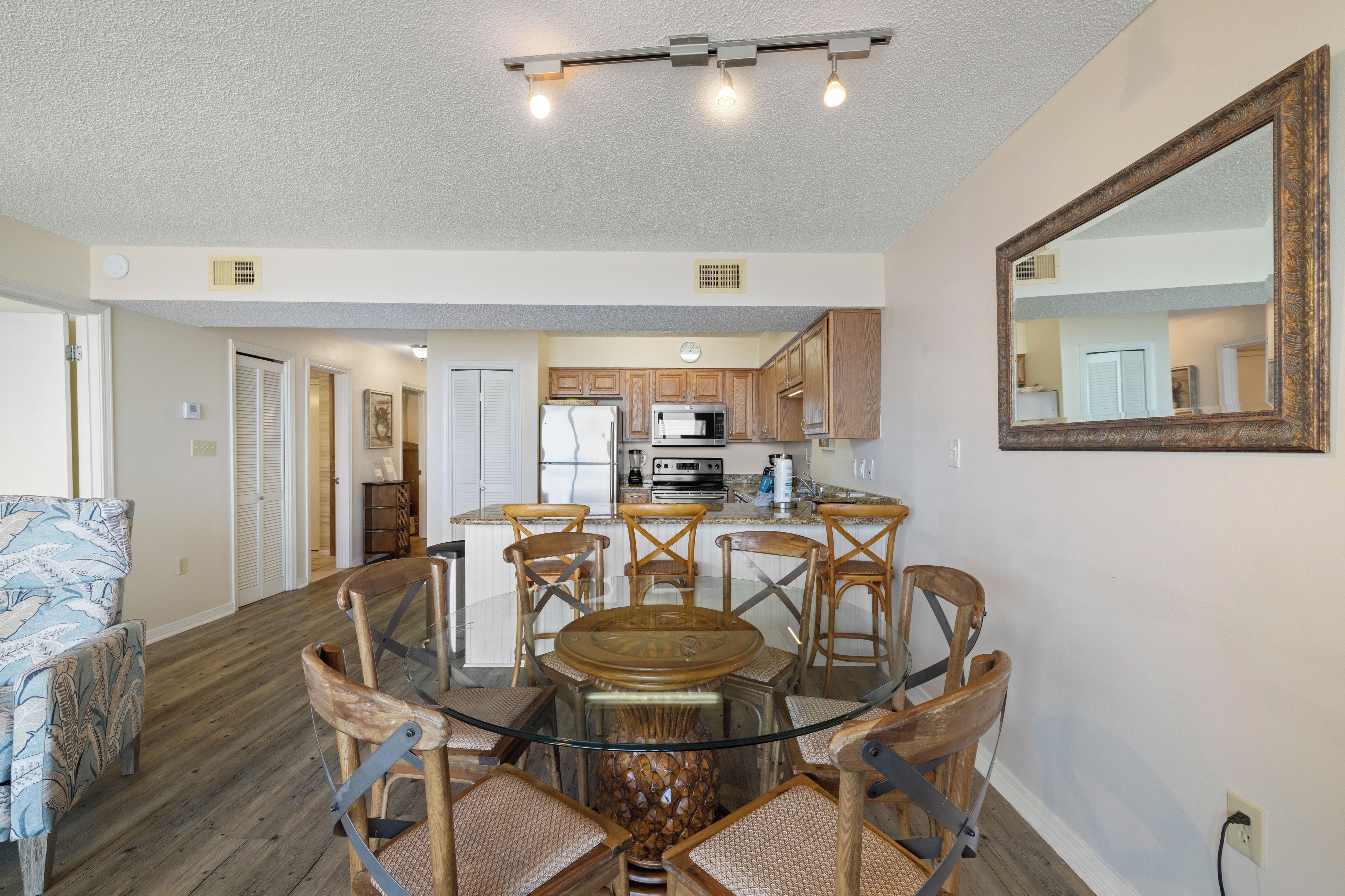 Una cocina moderna con armarios de madera, una isla central y un comedor con mesa de vidrio y sillas de madera.