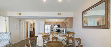 Una cocina moderna con armarios de madera, una isla central y un comedor con mesa de vidrio y sillas de madera.