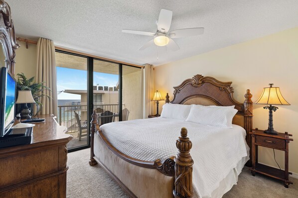 A hotel room with a large bed, a ceiling fan, a desk with a computer, and a view of the sea through a sliding door. - Seaside Beach & Racquet 5915 by Liquid Life (Orange Beach)