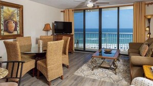 A room with a balcony, a television, wicker furniture, and a view of the ocean. - Seaside Beach & Racquet 5915 by Liquid Life (Orange Beach)