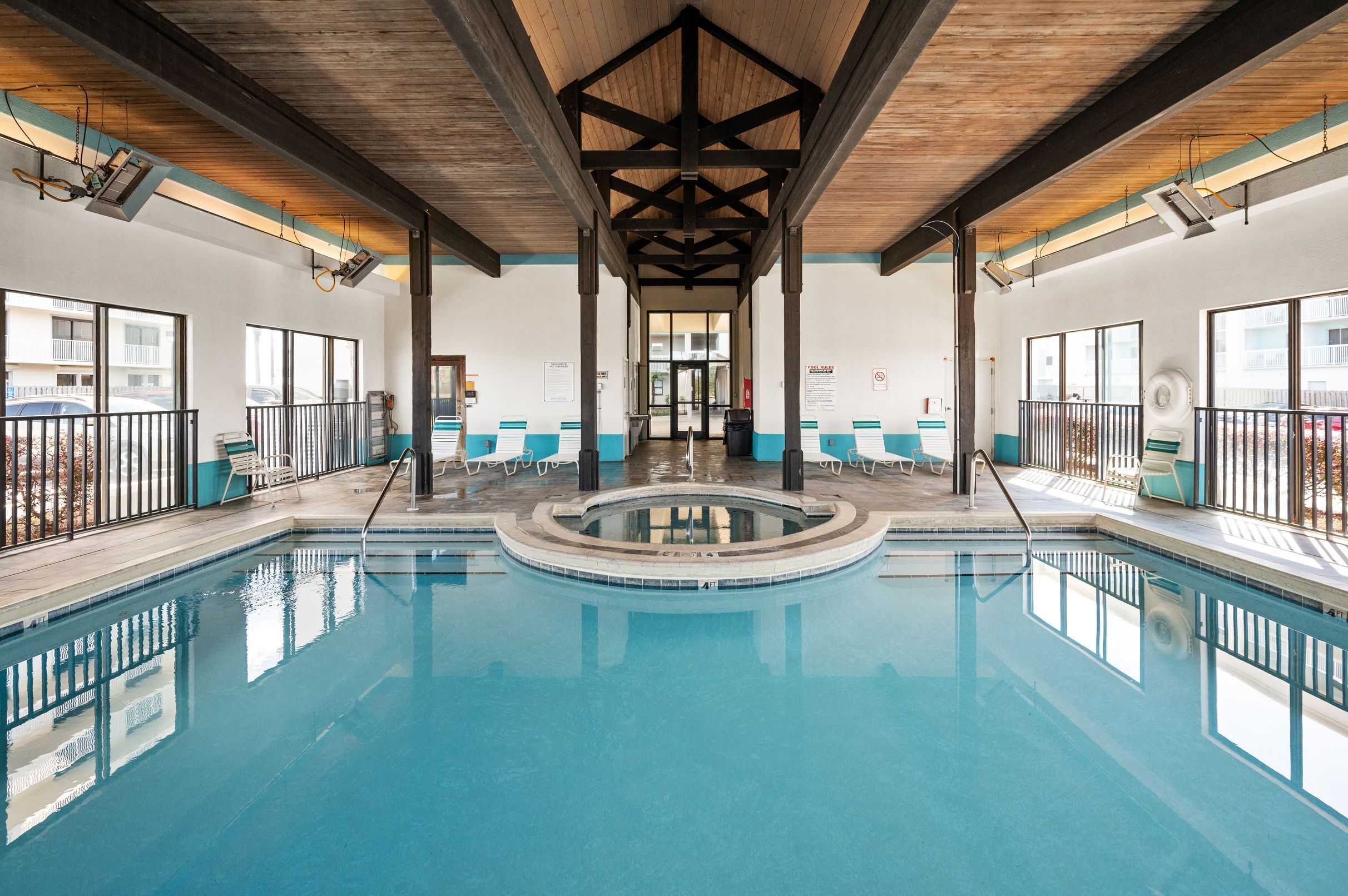 An indoor swimming pool with clear water, surrounded by lounge chairs and a wooden ceiling structure.