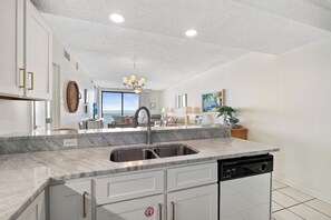 A modern kitchen with a large island, built-in dishwasher, and a view to the outside. - Shoalwater 604 by Liquid Life (Orange Beach)