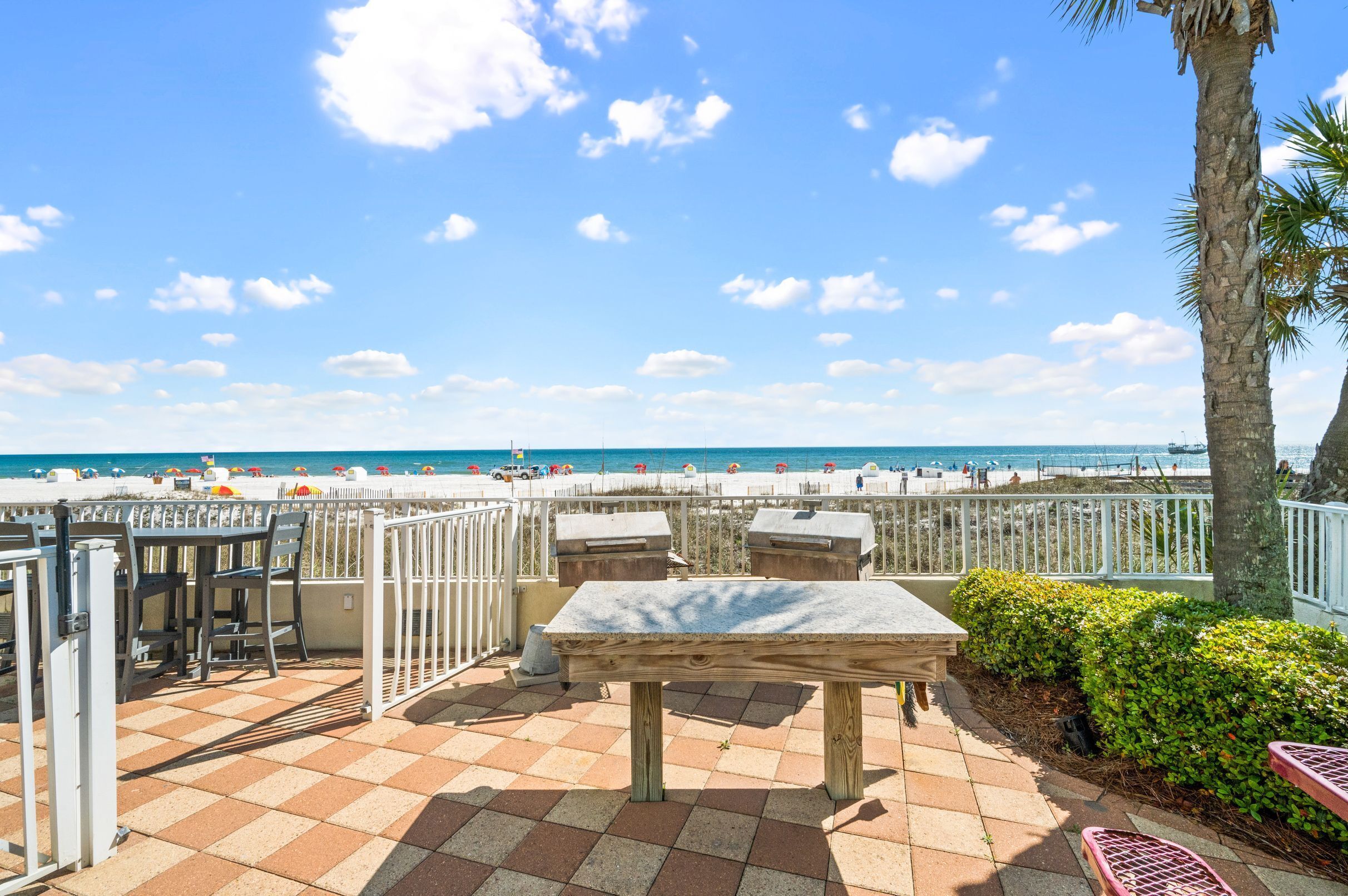 A beachside patio with a view of the beach, a grill, and a table.