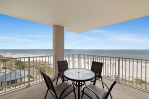 Un balcon avec une table et des chaises, donnant sur une plage parsemée de parasols et fréquentée par des gens.