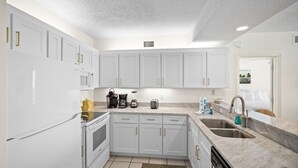 A modern kitchen with white cabinetry, a built-in oven, a microwave, and a coffee maker. - Shoalwater 604 by Liquid Life (Orange Beach)