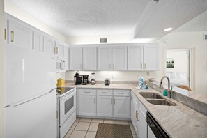 A modern kitchen with white cabinetry, a built-in oven, a microwave, and a coffee maker. - Shoalwater 604 by Liquid Life (Orange Beach)