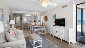 A modern living room with a sofa, a dining table with chairs, a TV, and a ceiling fan. - Shoalwater 604 by Liquid Life (Orange Beach)