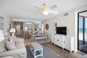 A modern living room with a sofa, a dining table with chairs, a TV, and a ceiling fan. - Shoalwater 604 by Liquid Life (Orange Beach)