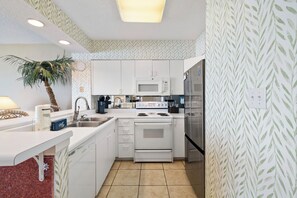 A compact kitchen with white cabinetry, a built-in oven, a microwave, and a refrigerator. - Silver Beach 203 by Liquid Life (Orange Beach)