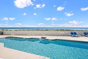 A clear blue pool with a diving board, lounge chairs, and a view of the ocean. - Silver Beach 203 by Liquid Life (Orange Beach)