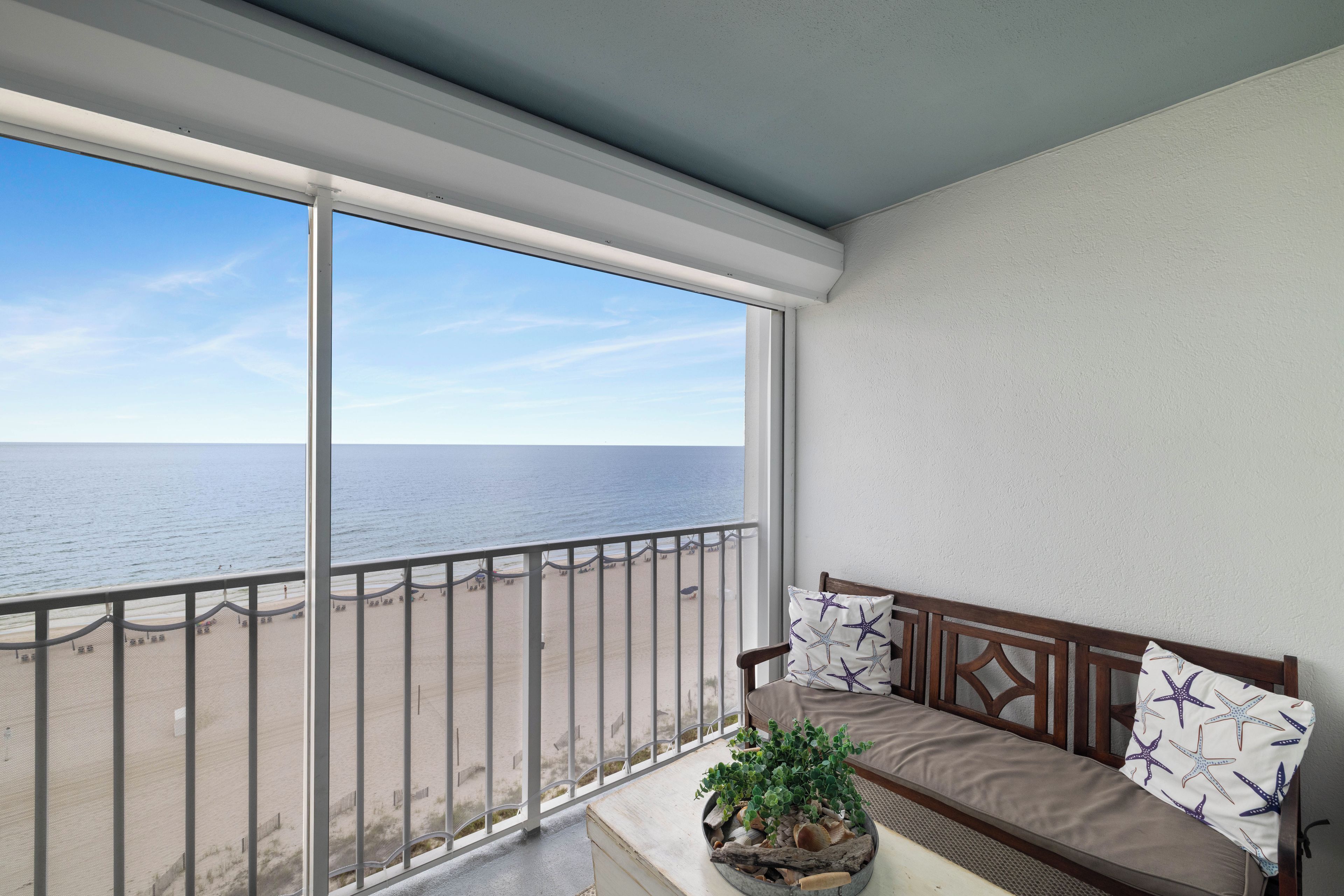 A balcony with a view of the sea, a wooden bench, and a potted plant.