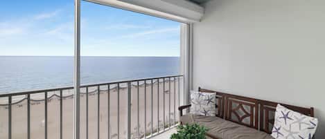 A balcony with a view of the sea, a wooden bench, and a potted plant.