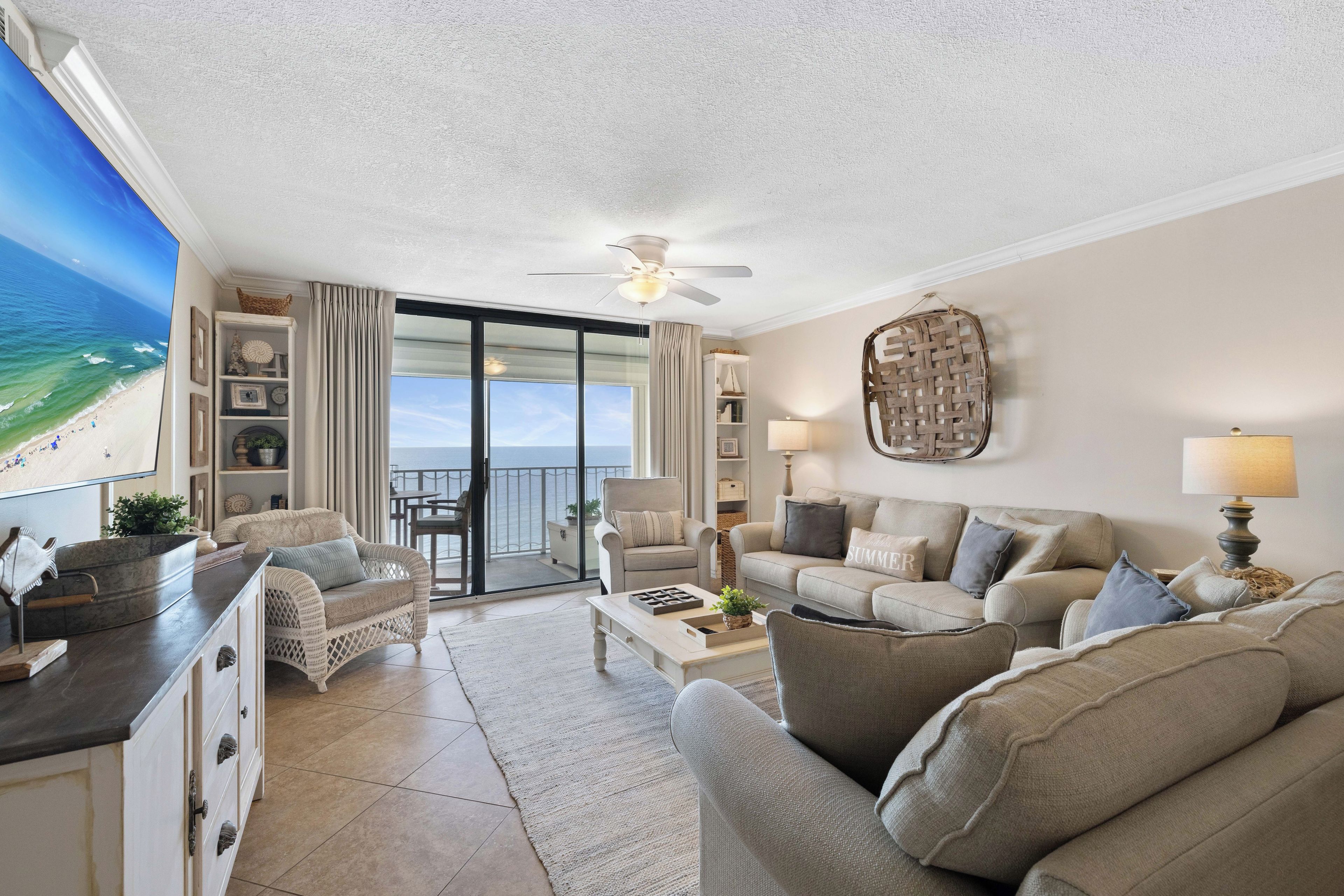 Een woonkamer met uitzicht op het strand, een plafondventilator en een groot raam.