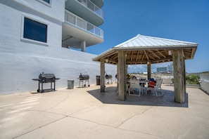 Eine Terrasse im Freien mit einem Pavillon, Grillanlagen und Blick auf ein weißes Gebäude mit Balkonen.