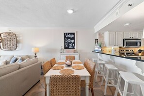 A compact living space with a dining area, kitchenette, and a wall-mounted sign. - Summerchase 803 by Liquid Life (Orange Beach)