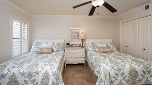 Quarto com duas camas, mesa de cabeceira, ventilador de teto e uma porta.