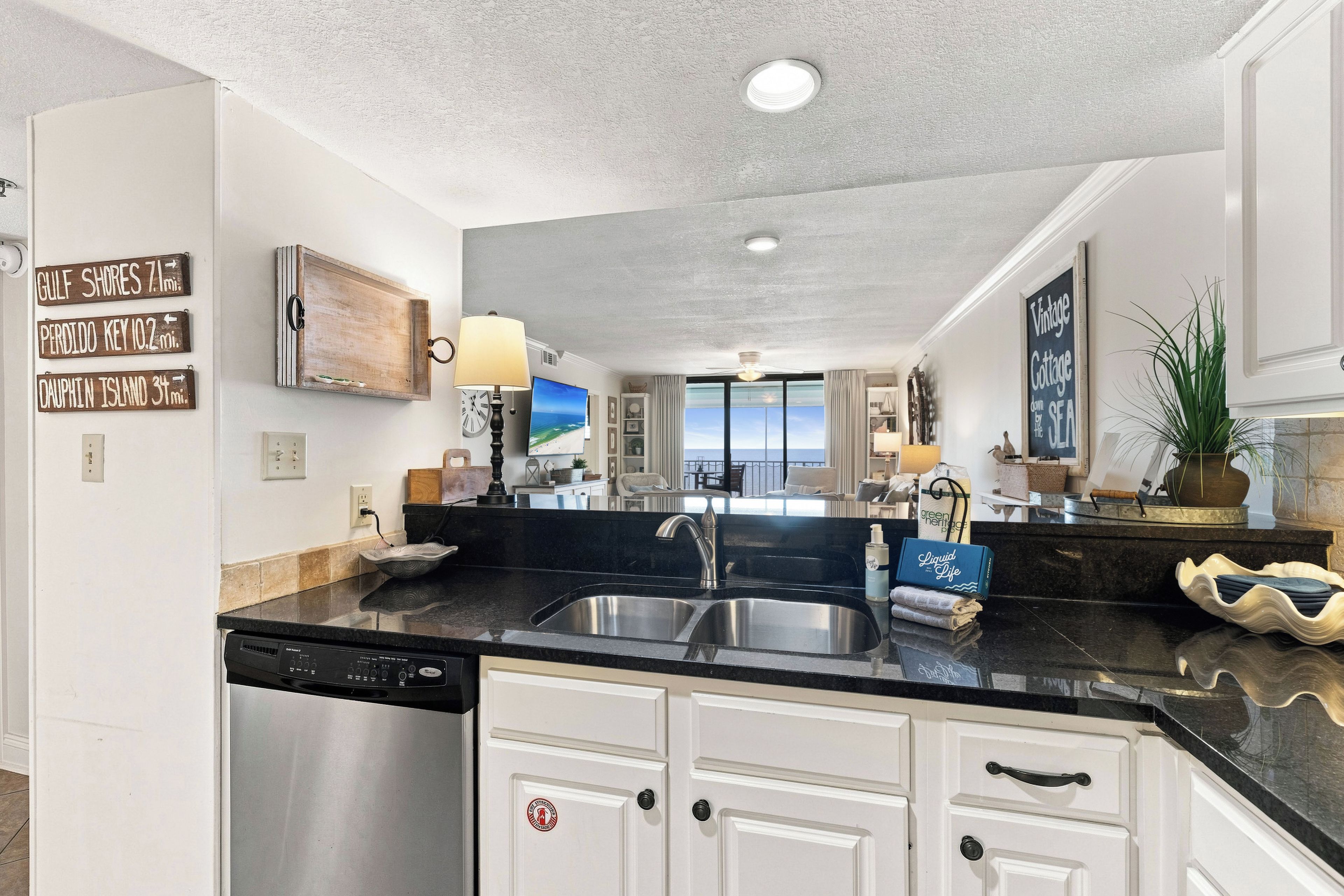 A modern kitchen with a dishwasher, double sink, and a view to the living area.
