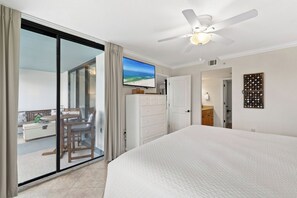 Ein Hotelzimmer mit einem großen Bett, einem Deckenventilator, einem an der Wand befestigten Fernseher und einer Glastür, die auf einen Balkon mit Gartenmöbeln führt.