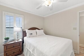 A bedroom with a bed, a nightstand, a lamp, a ceiling fan, and a window with blinds. - Summerchase 803 by Liquid Life (Orange Beach)