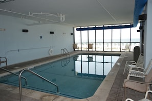 Ein Hallenbad mit klarem, blauen Wasser, einem Sprungbrett und Blick auf den Strand durch große Fenster.