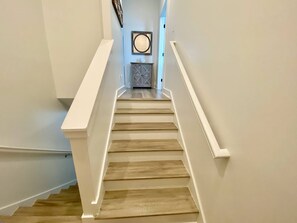 Una escalera con escalones de madera y barandas blancas, que conduce a una plataforma con un adorno mural y un armario.
