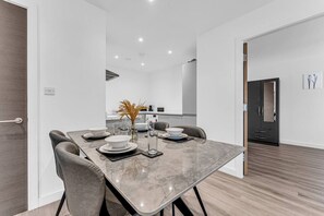 Un espace repas moderne avec une table en marbre, des chaises grises et un vase contenant des plantes séchées.