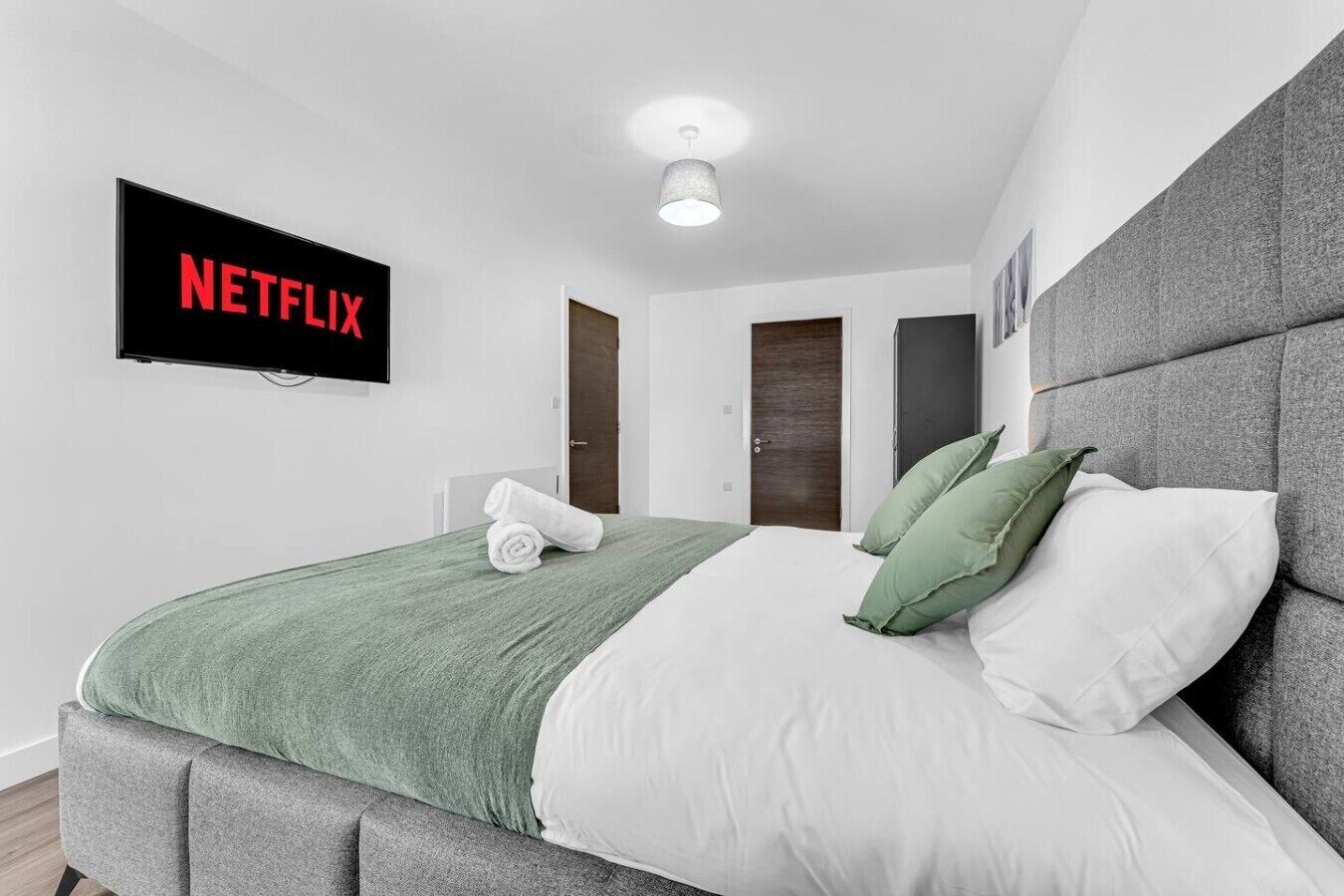 Een moderne hotelkamer met een bed, een flatscreen televisie aan de muur en een deur die naar een andere kamer leidt.