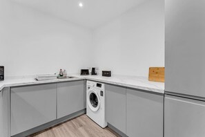 A modern kitchen with grey cabinets, a built-in washing machine, a countertop with a cutting board, and a sink. - Stylish & Spacious Anfield Flat | WiFi | Sleeps 4 (Anfield)