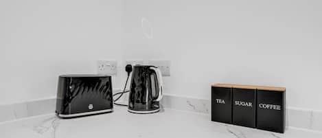 A kitchen counter with a toaster, a kettle, and three black boxes labeled tea, sugar, and coffee.
